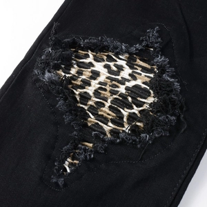 Detailed macro view of black denim pants featuring leopard print patches and frayed edges