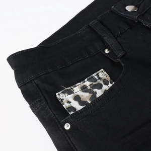 Detailed close-up of men's black jeans featuring leopard print pocket patch and metal rivets