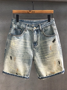 Detail view of light blue washed denim shorts with paint splatter and cuffed hems