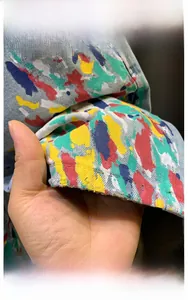 Detail of blue denim shorts featuring colorful paint splatter and frayed raw edges