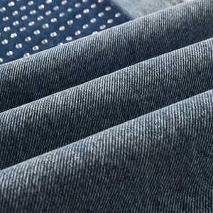 Macro detail of dark blue denim fabric with silver rhinestone studs and twill texture