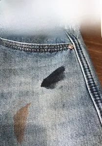 Detail of light blue washed denim shorts with graffiti art and metal rivets on the pocket