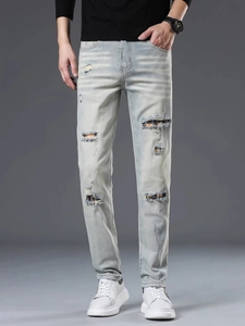 Detail view of men's ripped light blue jeans featuring vintage plaid fabric patches
