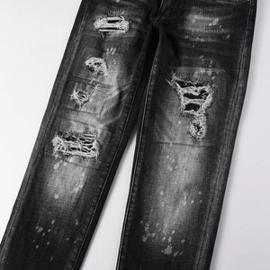 Detail of distressed dark grey jeans featuring heavy wash effects and white paint splatters