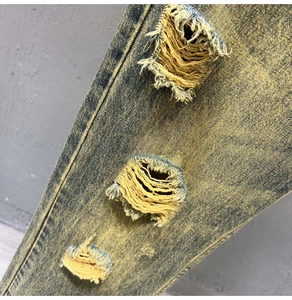 Detailed close-up of distressed ripped jeans featuring vintage yellow wash denim texture