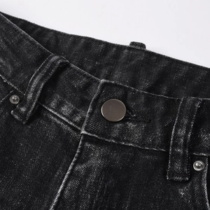Detailed close-up of distressed black washed denim jeans with matte metal button and stitching