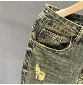 Macro shot of acid-wash denim jeans showing ripped distressing and metal rivet details