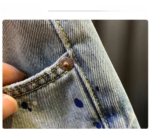 Macro view of light blue denim shorts featuring colorful paint splatters and copper studs
