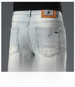 Detail of light blue denim back pocket with distressed edge and brown leather logo patch