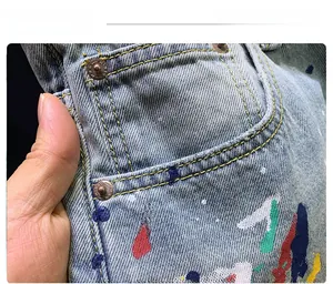 Detail of light blue washed denim shorts featuring multi-colored paint splatter and yellow stitching