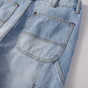 Detail of light blue washed denim back pocket with contrast stitching and metal rivets