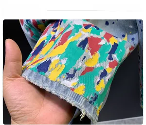 Close-up of light blue denim shorts featuring colorful graffiti paint and frayed hem detail
