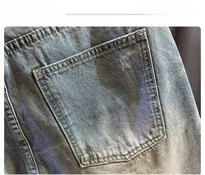 Detail of light blue denim back pocket with vintage wash, yellow stitching and distressed holes