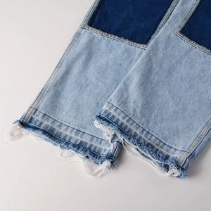 Close-up of dual-tone denim patchwork pants featuring raw hem fringes and orange stitching