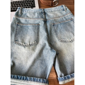 Rear view of men's washed light blue denim shorts with rolled cuffs on wood background