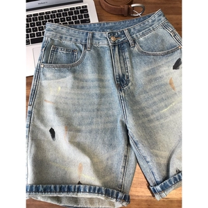 Vintage light blue washed denim shorts with artistic paint splatters on wooden desk