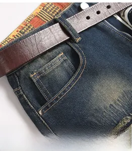 Close-up of front pocket on distressed blue denim jeans with detailed stitching and leather belt