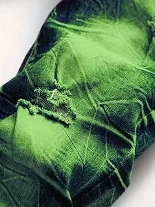 Vue détaillée des effets déchirés et du délavage tie-dye sur le jean slim vert pour homme