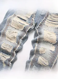 Detail of light blue distressed denim jeans with heavy fraying and wave embroidery motifs