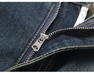 Detailed close-up of heavy-duty metal zipper and orange stitching on dark blue denim jeans