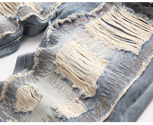 Close-up of distressed light blue jeans with fringe holes and zigzag embroidery detail