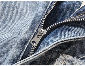 Macro detail of silver metal zipper and frayed fringe edges on vintage denim jeans