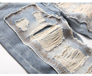 Detailed close-up of distressed denim with orange Z-shaped stitching and frayed edges