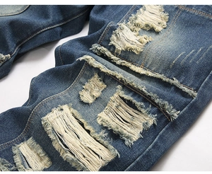Macro detail of distressed blue denim jeans with ripped holes and white frayed thread