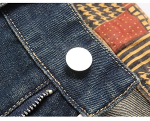 Macro detail of men's distressed jeans featuring metal button and colorful patch details