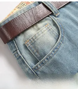 Detail of light blue denim front pocket and leather belt with yellow double stitching