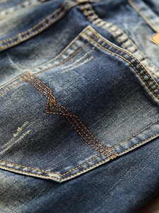Detail of vintage washed blue denim jeans with contrast orange stitching on back pocket