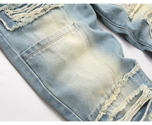 Detail of light blue distressed jeans featuring vintage yellow wash and frayed rip effects