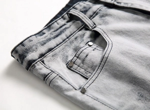 Dettaglio macro del denim snow wash con rivetti su jeans strappati da uomo