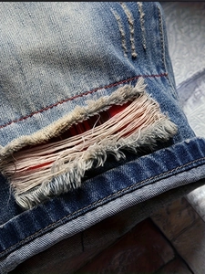 Men's blue distressed denim shorts with heavy ripped detail and red inner lining