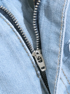 Close-up of silver metal zipper and yellow stitching on light blue denim shorts