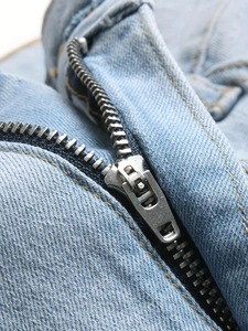 Dettaglio della cerniera in metallo e cuciture gialle su pantaloncini di jeans blu