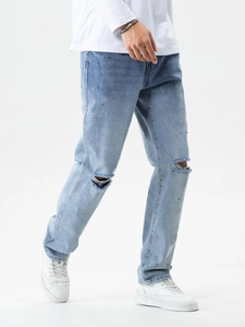 Detail der hellblauen Jeans mit Distressed-Knielöchern und schwarzen Farbspritzer-Akzenten