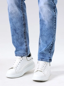 Jean coupe slim bleu clair délavé pour homme porté avec baskets blanches à plateforme