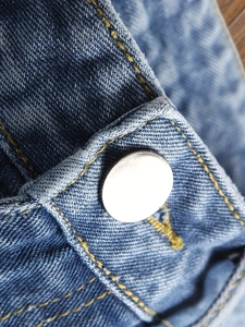 Gros plan sur un jean bleu délavé avec bouton métallique poli et coutures jaunes contrastées