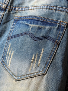 Detail of light blue straight jeans back pocket with wash effect and ripped denim fabric