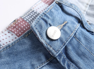 Détail du short en jean avec bouton argenté gravé et coutures jaunes contrastées classiques