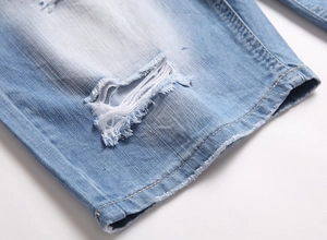 Detailed macro view of light blue denim fabric featuring ripped holes and frayed edges