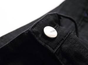 Macro d'un bouton de jean en argent embossé sur un tissu denim sergé noir de qualité