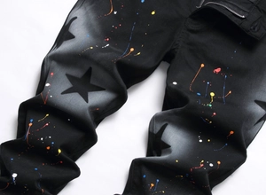 Detail shot of black slim fit jeans featuring artistic colorful paint splatter and star print