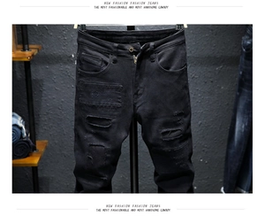 Close-up of black slim fit jeans featuring worn-out patches and distressed hole details