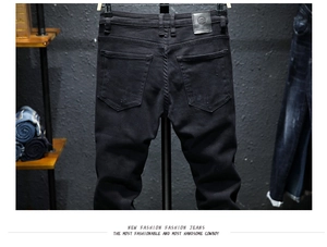 Detail of slim black jeans featuring back pockets with subtle distress and leather waist patch