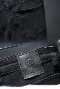 Detail of ripped back pocket and leather brand patch on slim black men's jeans