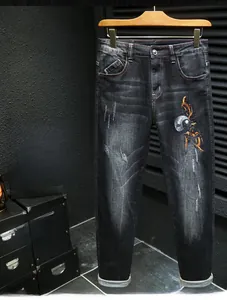 Gros plan sur un jean en denim noir avec broderie de scorpion et finition délavée