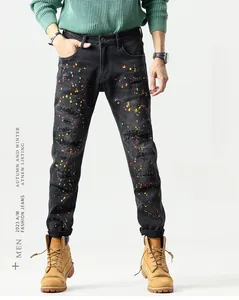 Detail of slim fit distressed black denim jeans with colorful paint splatters and ripped fringe