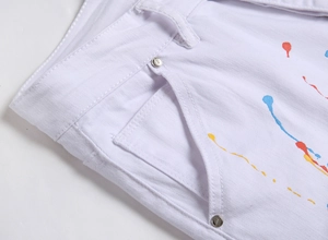 Nahaufnahme weißer Jeans mit bunten Farbspritzern und Metalldetails an den Nieten